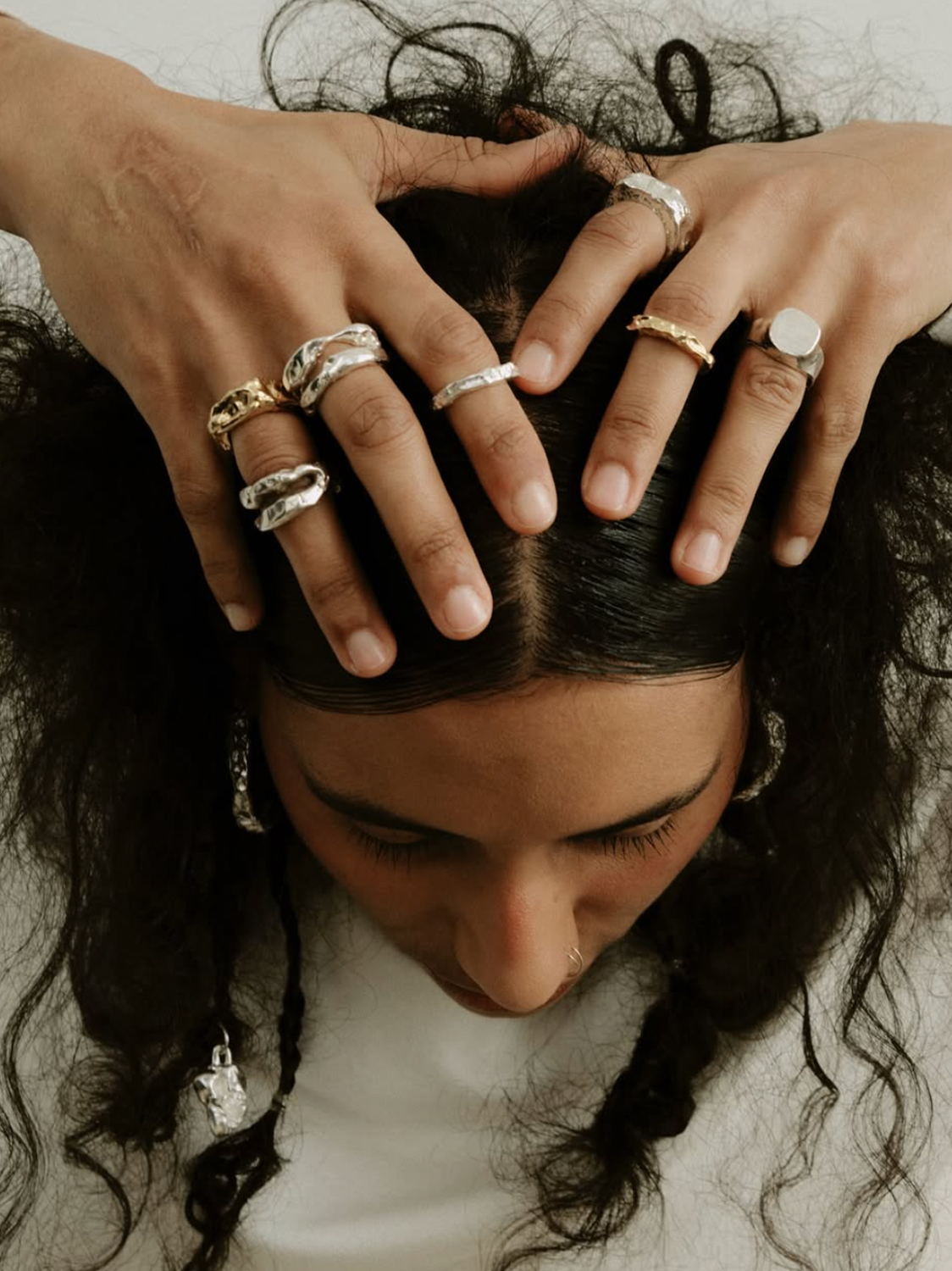 Primer plano editorial de una modelo con las manos y anillos sobre el cabello.