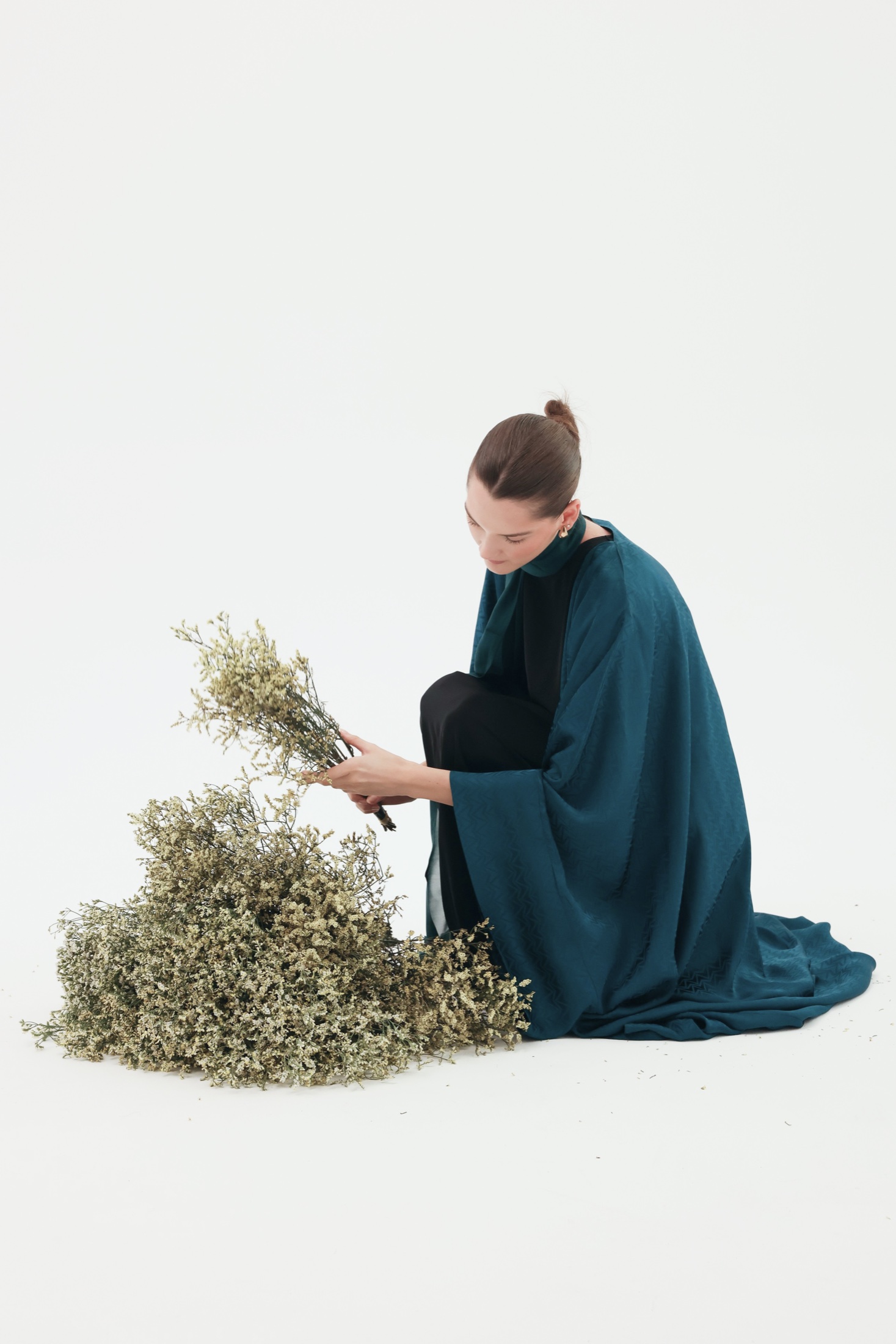 Model in a teal abaya arranging dried flowers.