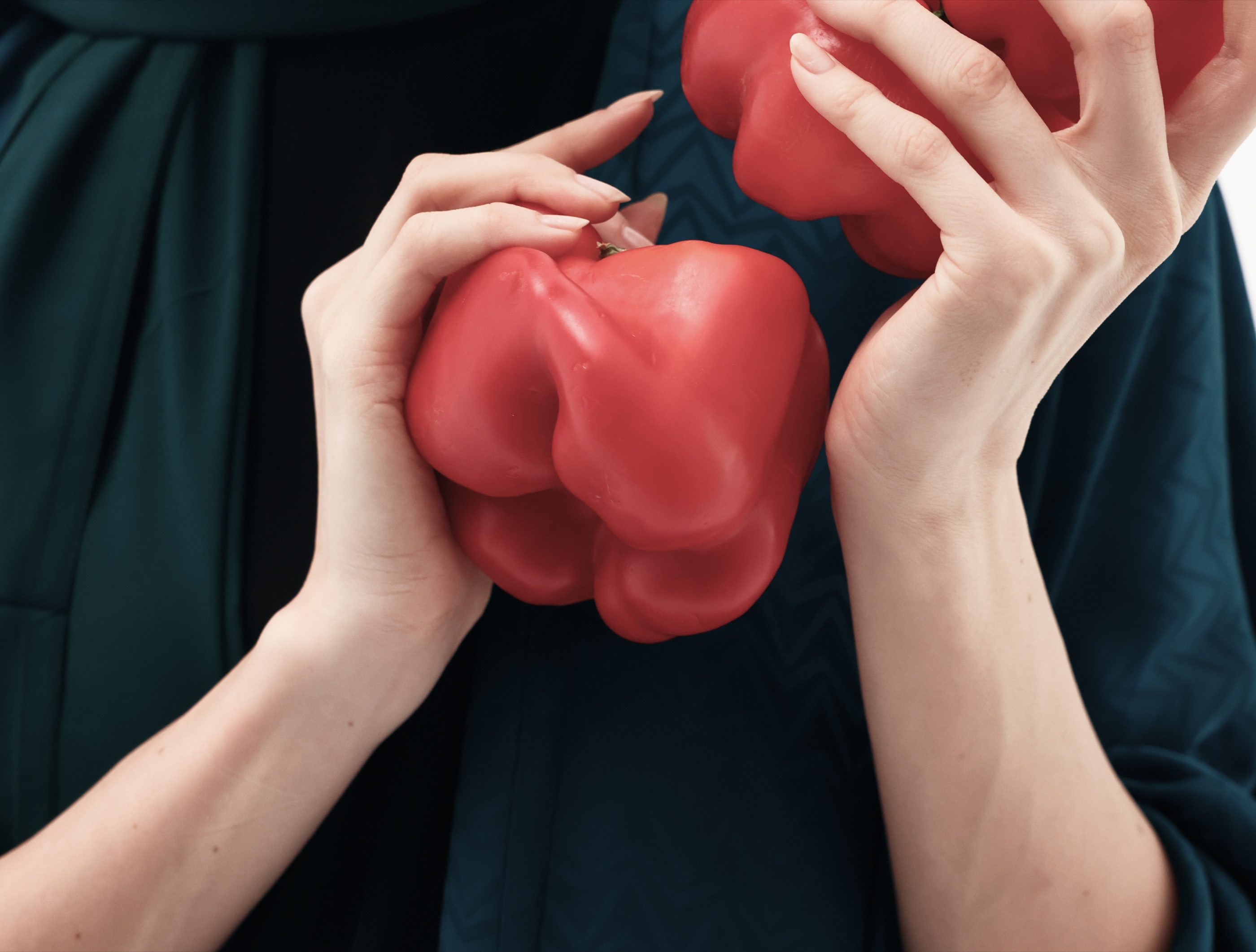 Close-up of a model in a teal abaya holding red peppers.