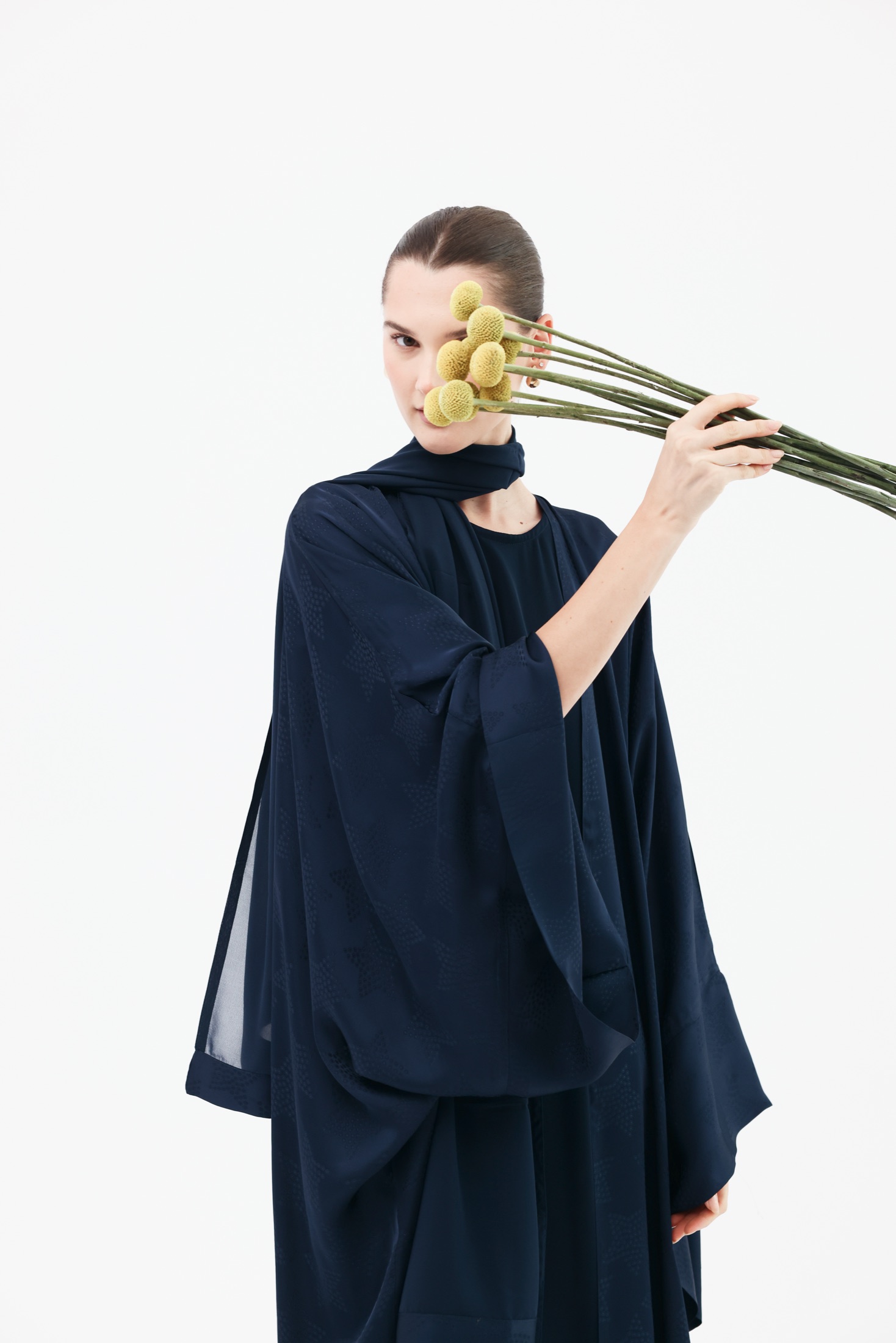 Model holding yellow flowers across her face.