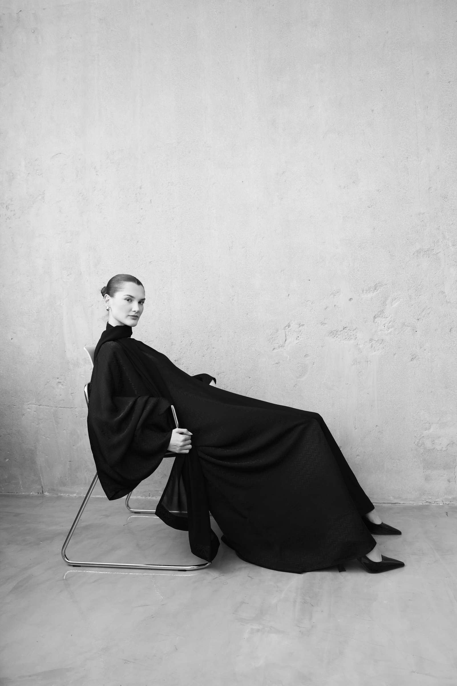 Tre Sorelle campaign: model seated in a black abaya against a textured wall.